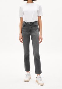 Vaqueros de tiro alto y pierna recta en denim gris oscuro, con bolsillos delanteros y detalles sutilmente desgastados, combinados con una camiseta blanca y zapatillas.