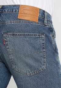 Levi's blå jeans i denim med en läderlapp bak, med klassiska sömmar och en enda röd flik på bakfickan.