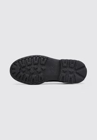 Semelle en caoutchouc noir avec des rainures profondes, des motifs floraux et rectangulaires, et le logo "Fluchos" embossé au centre.