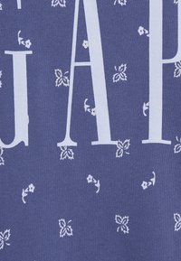 Tejido azul con letras parciales grandes en blanco y un patrón disperso de pequeños motivos florales y de hojas en blanco.
