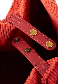 Bolsa de pana roja con asas de cuero que presenta herrajes dorados y cierres a presión. Textura suave con un diseño acanalado en la parte superior.