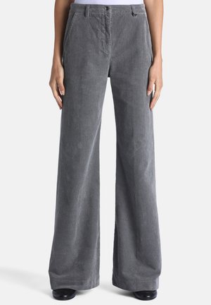 Pantalon en velours côtelé gris à jambes droites avec fermeture par bouton et fermeture éclair, porté avec des chaussures noires et un haut blanc.