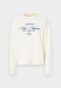 Sweatshirt crème à col rond, avec un texte brodé bleu : "GANT 1949 New Haven Sailing Crew 06516 CT. USA." Design simple.