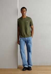 Olivengrøn bomulds t-shirt med et lille logo, parret med lyseblå denimjeans. Sorte sko fuldender det afslappede outfit.