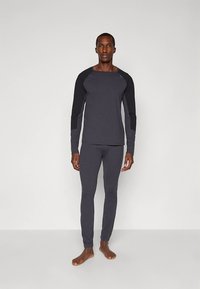 Długi rękaw sportowy top i dopasowane spodnie w ciemnoszarym kolorze, z kontrastującym czarnym wzorem na ramieniu, elastyczną tkaniną i gładką fakturą.