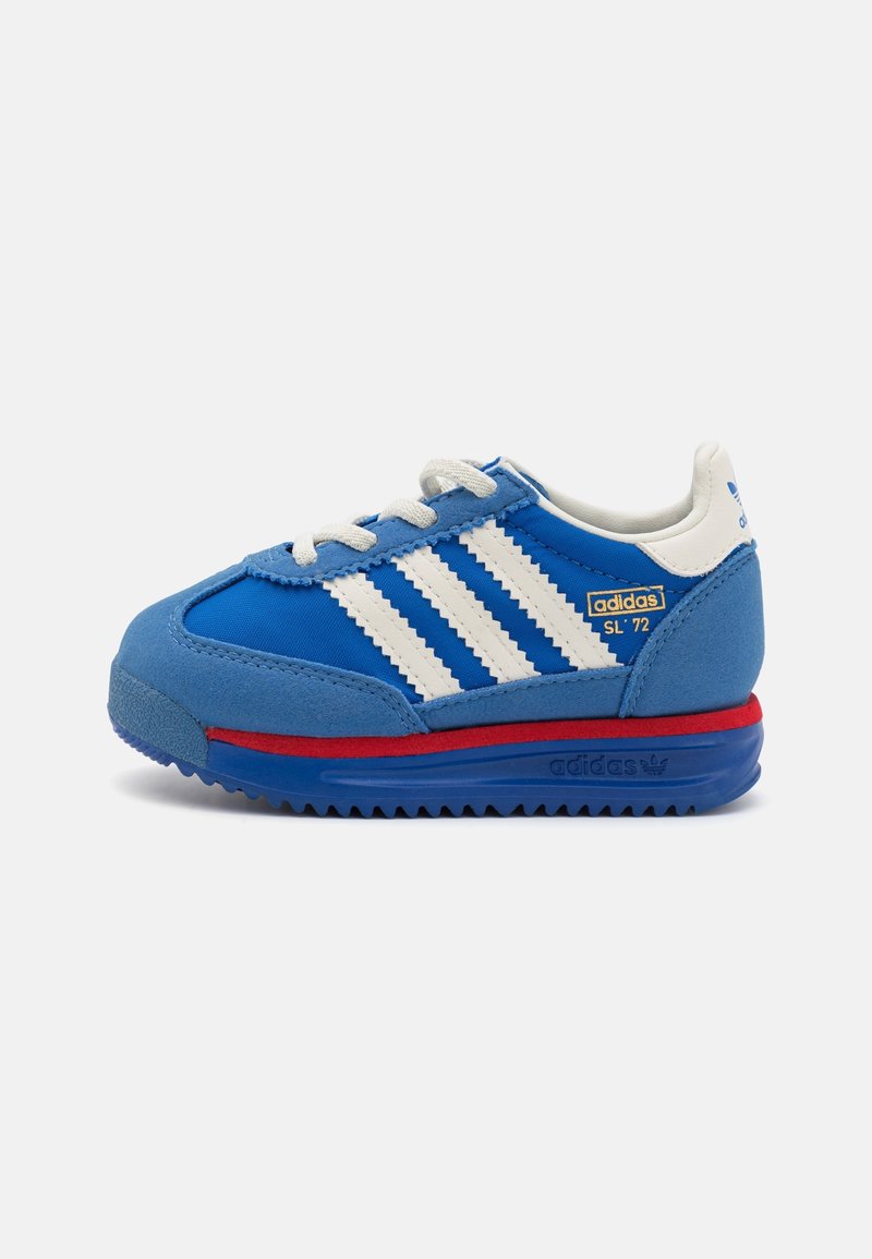 Blue sneaker with suede and fabric upper, white three stripes, red midsole accent, round laces, and rubber outsole. Features an adidas logo.