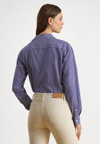 Modrá námornícka a biely pruhovaný košeľový top s dlhými rukávmi, vybavený klasickým golierom a svetlo béžovými nohavicami s zadnými vreckami a značkovou štítkom.