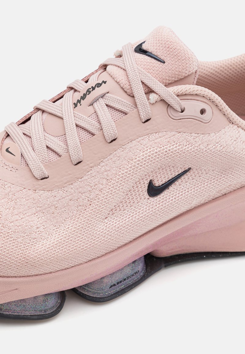 Hellrosa Sportschuh mit strukturierter Oberseite, schwarzem Nike-Logo und Air Zoom Dämpfung in der Sohle. Die Schnürsenkel sind im gewebten Design.