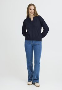 Marineblaues Langarm-Oberteil mit V-Ausschnitt, kombiniert mit weit geschnittenen blauen Jeans und hellen Sneakern. Glatter Stoff, legere Passform.
