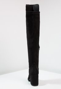 Bota negra por encima de la rodilla de ante con acabado liso, con un tacón grueso alto y un detalle de cremallera en el lateral.