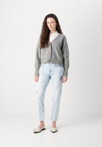 Grå ribbestrikket cardigan med messingknapper, hvit skjorte med krage, lyseblå jeans med blomsterbroderi og kremfargede leiligheter med bånddetalj.