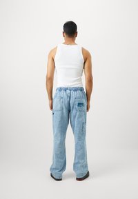 Világoskék farmer cargo nadrág rugalmas derékrésszel, hátul zsebekkel és laza fazonnal, fehér top-pal párosítva.