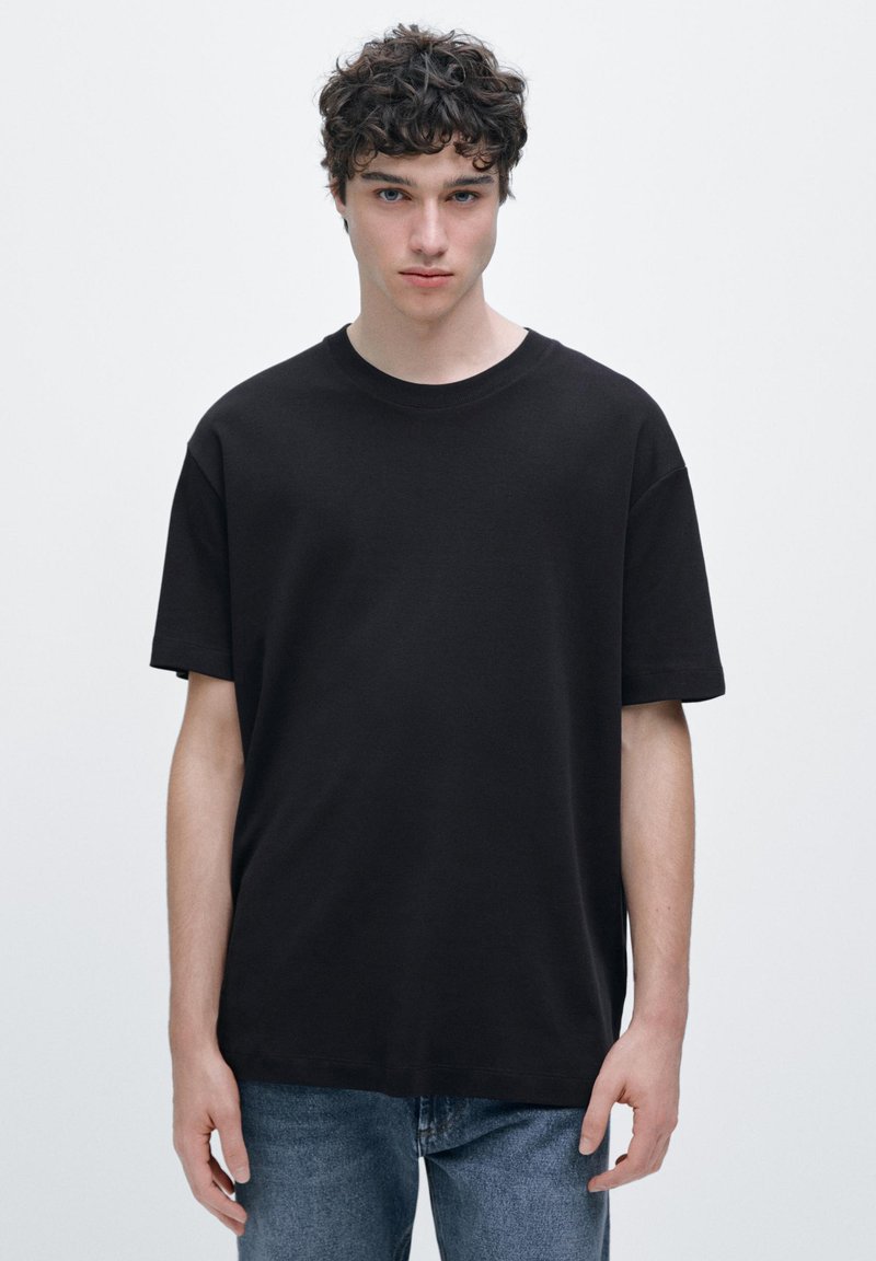 Svart t-shirt i bomull med rund halsringning och korta ärmar, kombinerad med blå jeans i denim. Enkel design, avslappnad passform, inga synliga mönster.