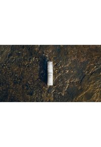 Flacon blanc de crème pour le visage Susanne Kaufmann avec pompe, posé sur une surface en pierre brun foncé texturée, centré et aligné verticalement.