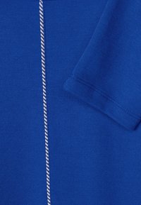 Ljust blått tyg med en slät textur, som har en vit dekorativ söm längs mitten och en kort, vikt ärm.