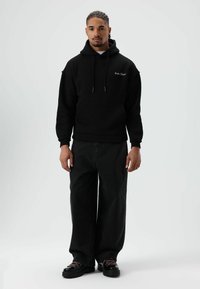 Zwarte hoodie met trekkoorden en een voorzak, gecombineerd met zwart spijkerbroek met een losse pasvorm en zwarte sneakers met roze accenten.