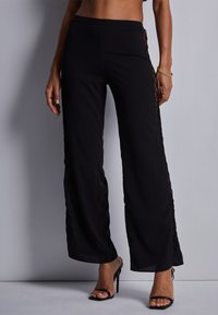 Pantalons noirs à jambe large avec un panneau latéral texturé et des découpes en forme de diamant. Fabriqués à partir d'un matériau léger avec une finition lisse.