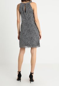 Musta-valkopilkkuinen mekko, jossa on olkaimeton muotoilu ja avainaukko takana, valmistettu kevyestä kankaasta ja ulottuu juuri polven ylle.