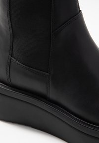 Botine negre din piele, cu panouri elastice pe laterale, textură netedă, talpă groasă și cusături detaliate pe găuri.