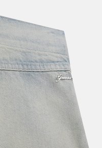 Timp de material denim bleu deschis, cu un accent logo argintiu pe buzunarul din spate, cusături detaliate și o textură netedă.
