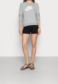 Grå Nike-tröja med vitt logotyp, svarta shorts och sandaler med djurmönster. Mjukt material, atletisk design och avslappnad passform.