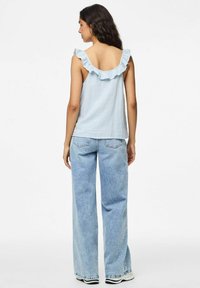 Ljusblå ärmlös topp med volangkrage, parat med högmidjade, vida ljus denimjeans. Slät textur och avslappnad passform.