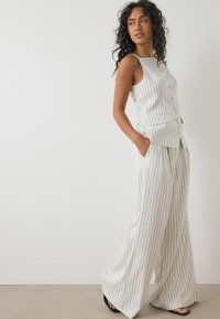 Lightweight, cream-colored, sleeveless top with vertical black stripes and buttons, paired with wide-leg matching trousers, also striped.