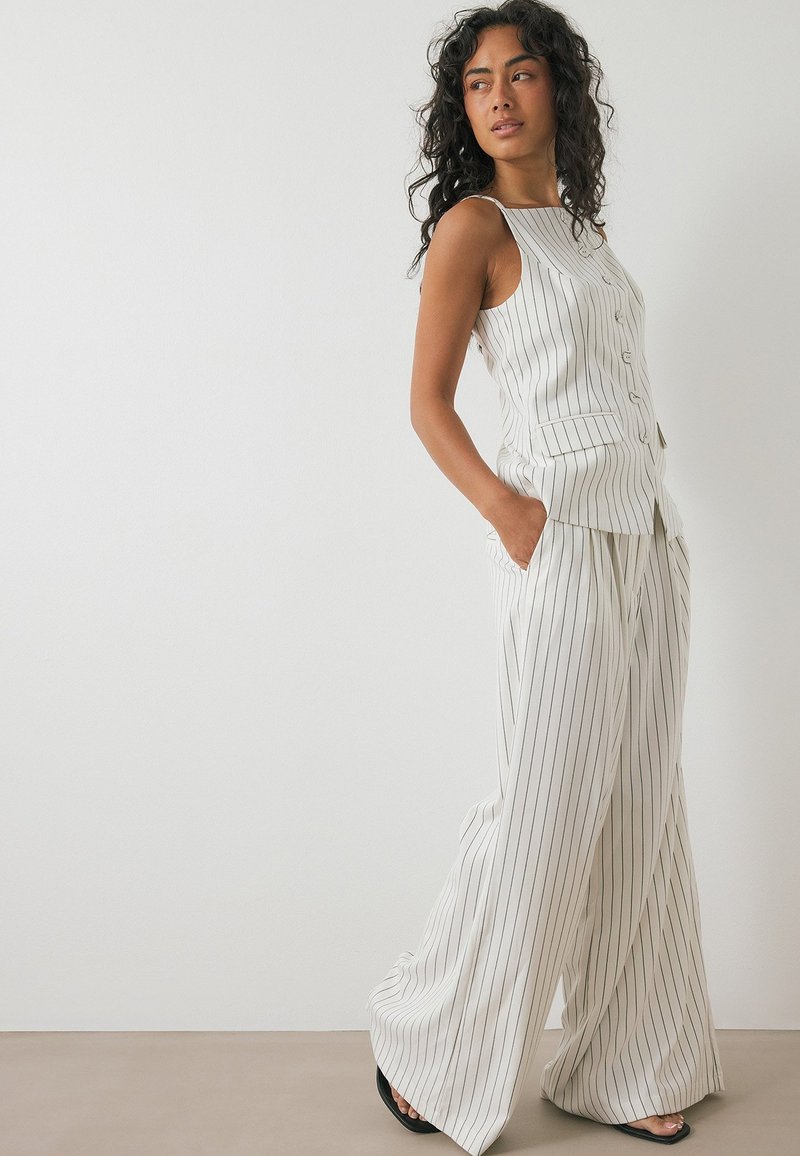 Lightweight, cream-colored, sleeveless top with vertical black stripes and buttons, paired with wide-leg matching trousers, also striped.