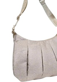 Beige skuldertaske lavet af tekstureret materiale, med draperinger foran, en tværgående rem og metalhardware.