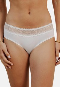 Culottes de bikini blanches en matériau lisse, avec une taille en dentelle à bords festonnés et des détails de motifs floraux.
