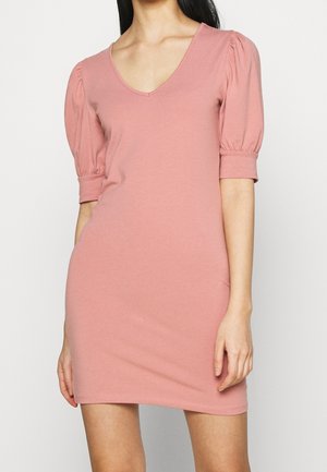Vrouw die een korte, stoffige roze jurk draagt met een V-hals en opgeblazen korte mouwen met aansluitende manchetten.
