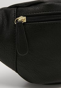 Pochette en cuir noir texturé avec une fermeture éclair dorée et une languette de tirette en cuir noir assortie.