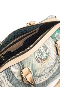 Patroon handtas met een crèmekleurige basis, donkere accenten en gouden hardware. Beschikt over een binnenzak en een ritssluiting voor veilige opberging.