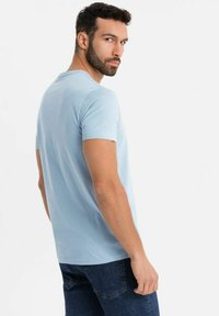 Camiseta de manga corta azul claro hecha de una tela suave, que presenta un escote redondo simple y un ajuste regular. Llevada con jeans oscuros.