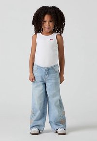 Vitt ribbat linne med liten röd logga, kombinerat med ljusblå vida jeans med blommig brodyr vid fållen och vita sneakers.