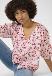 Blusa corta a maniche corte in tessuto rosa pallido, con motivi floreali rossi e gialli, scollatura a V e dettagli con bottoni.