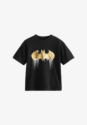 Svart bomullströja med en stor guldpaljett Batman-logotyp. Logotypen har droppande detaljer, korta ärmar och en rundad krage.