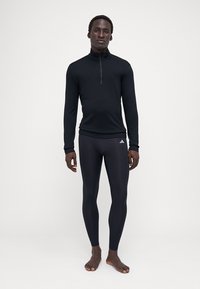 Schwarzes Langarmoberteil mit Viertelreißverschluss und eng anliegende schwarze Leggings, beide aus dehnbarem Stoff. Entworfen für aktive Kleidung.