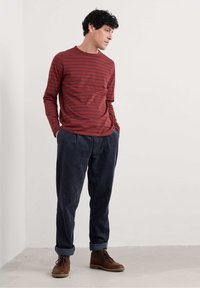 Punainen raidallinen pitkähihainen paita, joka on yhdistetty teksturoituihin tummansinisiin corduroy-housuihin ja ruskeisiin nauhallisiin saappaisiin. Yksinkertainen muotoilu, rento istuvuus.