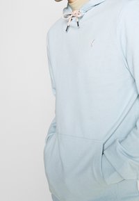 Felpa con cappuccio azzurro chiaro realizzata in tessuto morbido, dotata di tasca frontale, cordoncino regolabile con dettagli rosa e un piccolo logo ricamato.