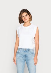 Camiseta branca, sem mangas, em algodão, com um decote redondo, combinada com jeans de ganga azul claro com um corte clássico e design de cinco bolsos.
