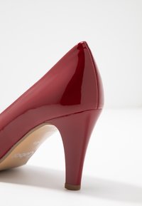 Décolleté rossa in pelle verniciata con punta affusolata, silhouette curva e tacco sottile. Superficie liscia e lucida con soletta color tan.