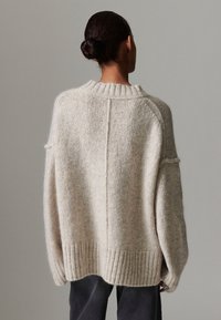 Suéter bege oversize feito de lã macia, com bainha e gola caneladas, ombros caídos e acabamento texturizado.