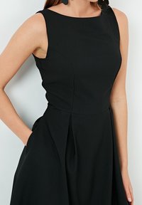 Černé bezramínkové šaty s přiléhavým korzetem, na bocích nařasené sklady v pase a boční kapsy, vyrobené z hladkého materiálu.