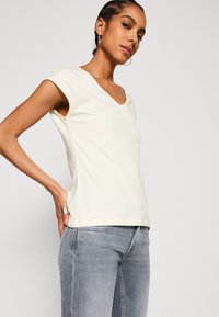 Crème-kleurige V-hals T-shirt met korte mouwen, gemaakt van zachte stof. Gecombineerd met lichtgrijze jeans, met een gestroomlijnd silhouet.