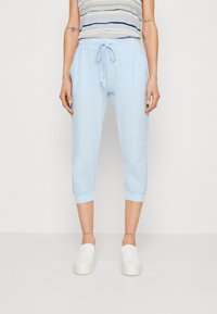 Lichtblauwe cropped broek met een trekkoord in de taille, voorzien van elastische manchetten en zijzakken. Gemaakt in combinatie met witte instappers.