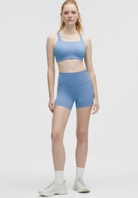 Ljusblå sportbehå med fyrkantig uringning och matchande högmidjade shorts. Slät textur, elastiskt tyg, figurnära design.