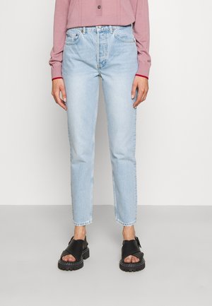 Jeans de tiro alto en azul claro con un corte recto, dobladillo deshilachado y diseño de cinco bolsillos, combinados con sandalias negras de plataforma.