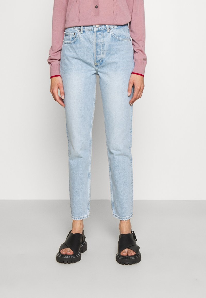 Jeans de tiro alto en azul claro con un corte recto, dobladillo deshilachado y diseño de cinco bolsillos, combinados con sandalias negras de plataforma.