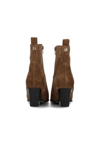 Botas de tobillo de ante marrón con un tacón cuadrado, que presentan un zipper lateral y un pequeño acento de logo en la parte trasera. Textura suave y forma redondeada.